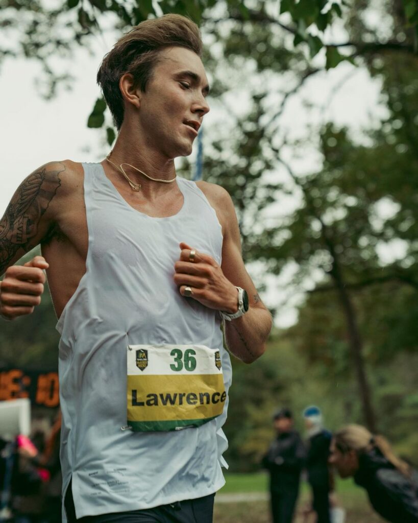 Ultra runner Charlie Lawrence runs with trees in the background while wearing a race bib
